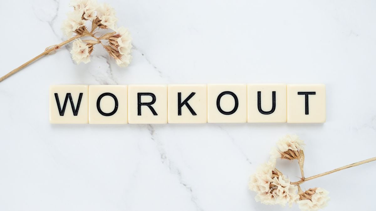 Letter tiles spelling 'WORKOUT' on marble with dried flowers, conveying fitness motivation.